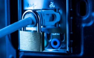 A closed padlock attached to a network cable plugged into the back of a computer to illustrate firewall cyber security solutions.