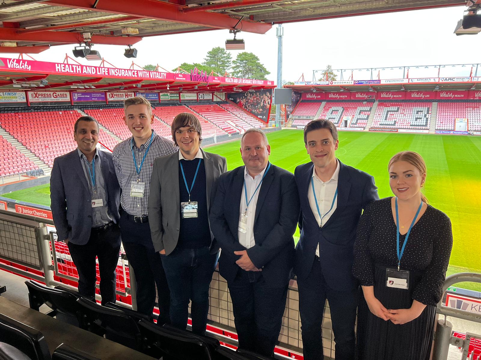 A photograph of staff from Grapevine and Gamma taken from the viewing boxes at AFC Bournemouth's stadium with the pitch and other stands in the background.